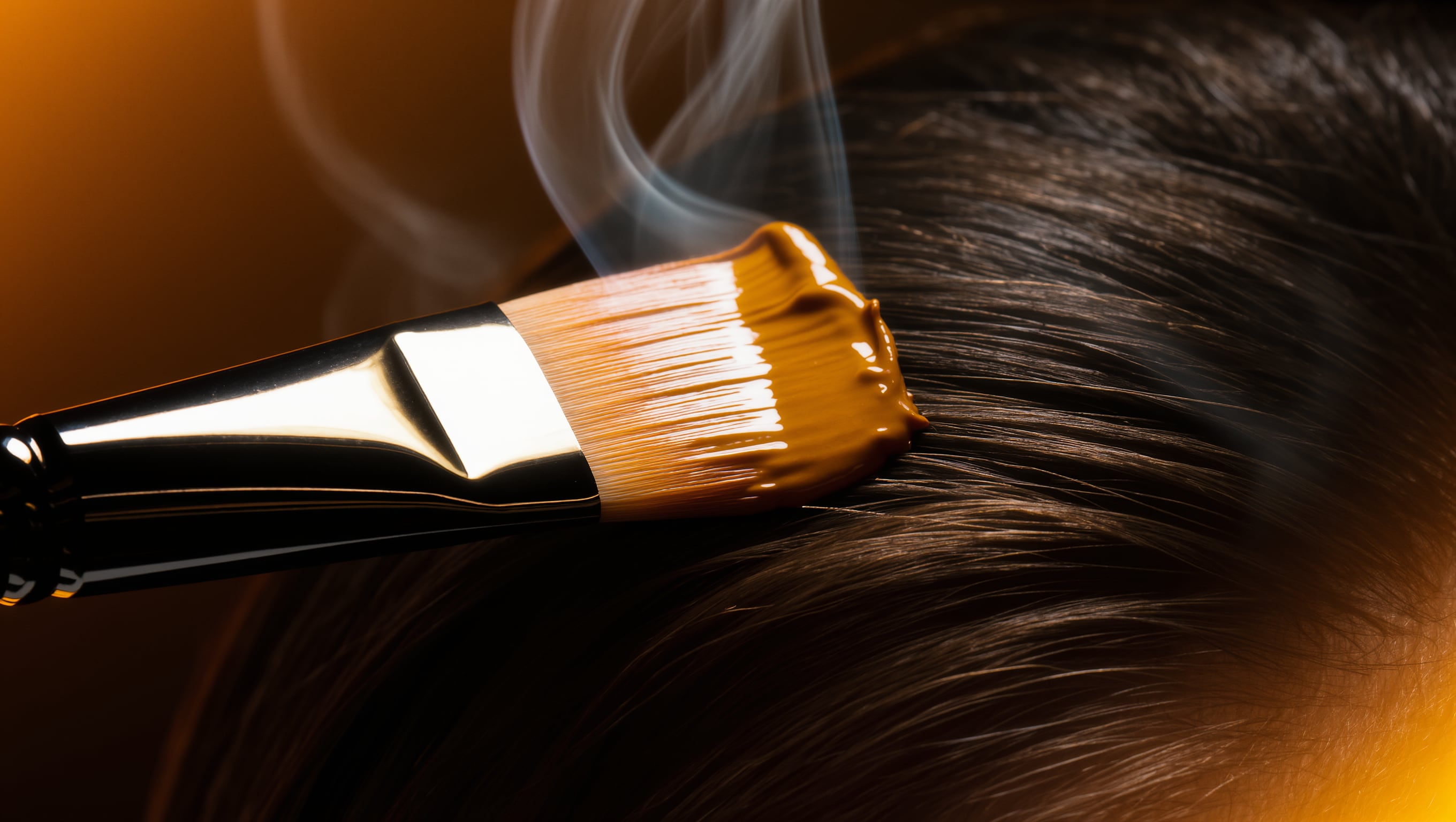 Cremige Haarmaske auf einem Pinsel ueber einer glaenzenden Straehne, Dampf und warmes Licht im dunklen Raum